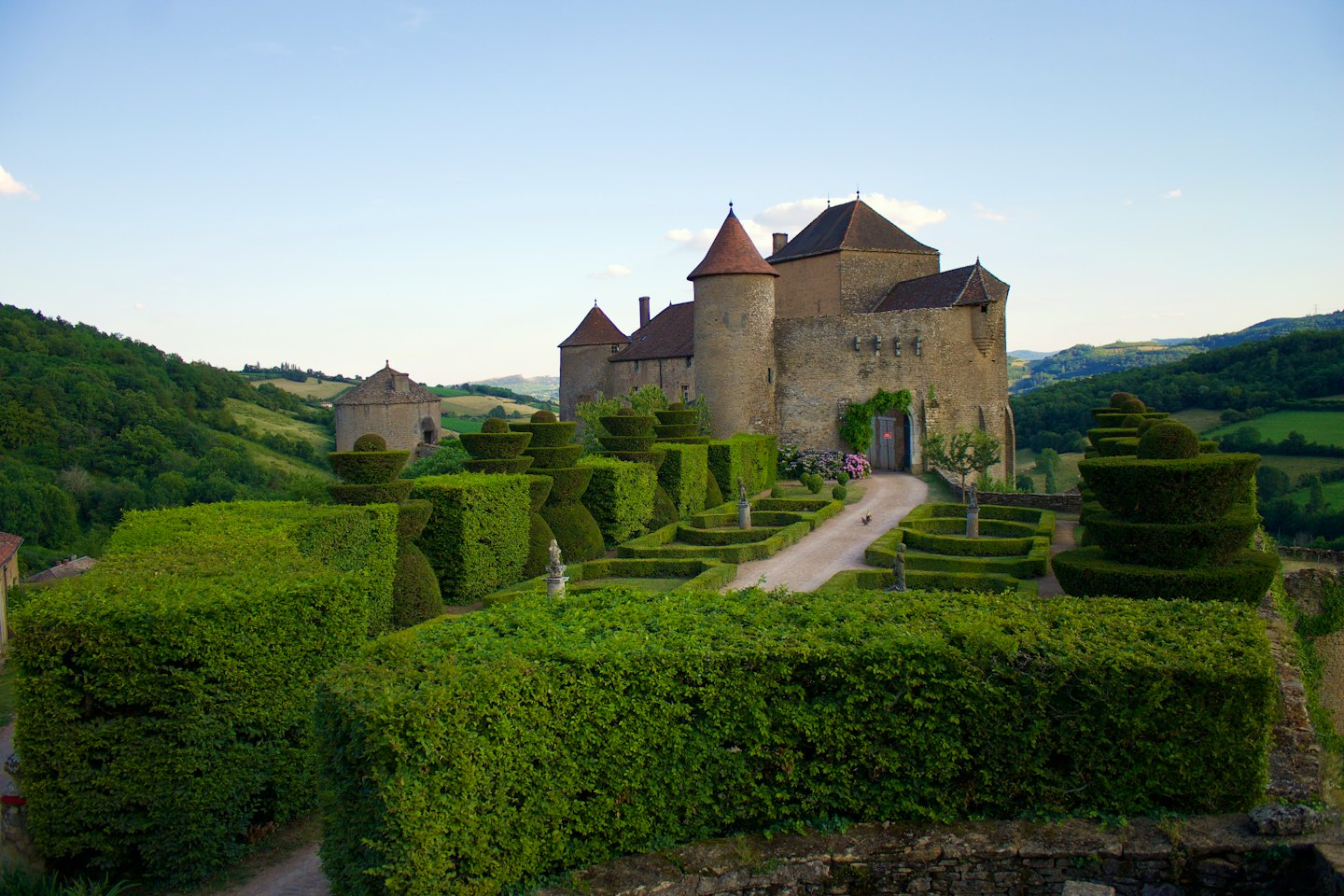 A stone castle with towers stands behind lush manicured gardens.