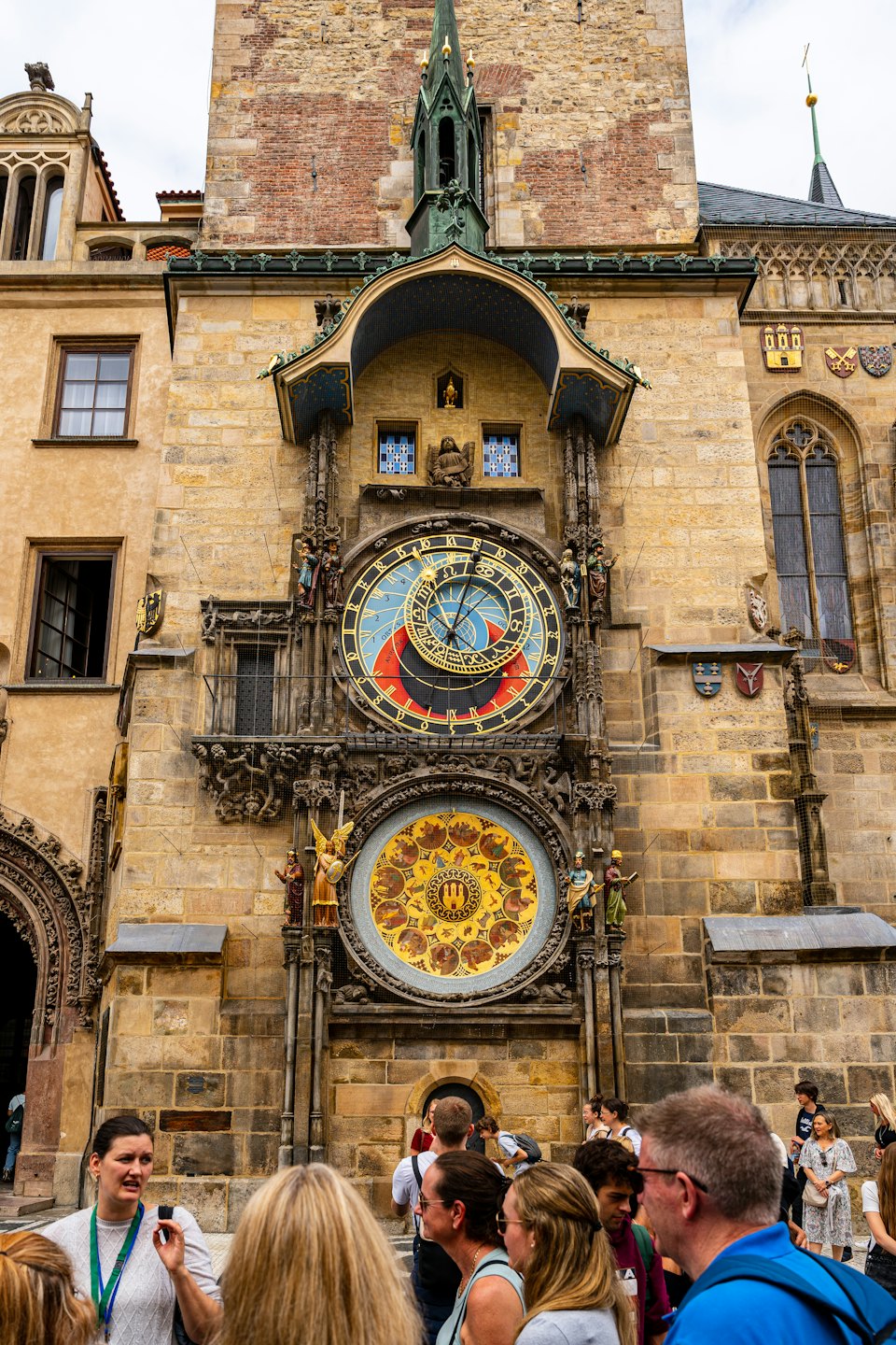 Tourists gather below the ornate astronomical clock on a historic building.
