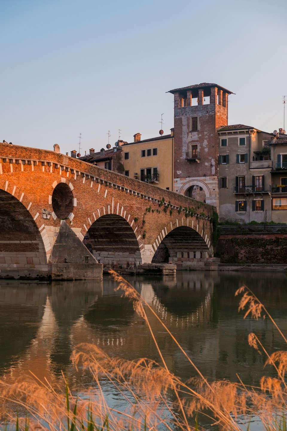 An ancient brick bridge arches over a river lined by historic buildings.